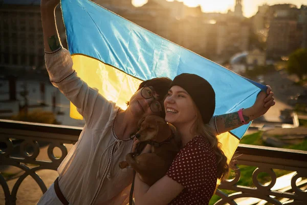 Gün batımında Kyiv 'in arka planında Ukrayna' nın sarı ve mavi bayrağını tutan genç kadınlar. Bir kız köpek kadar kaliteli bir fotoğraf tutuyor.