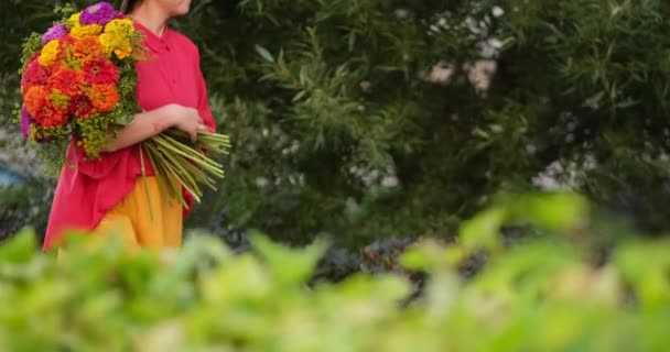 白人妇女拿着一束红色 橙色和黄色的菊花穿过花园 春天或夏天的概念 高质量的4K视频镜头 — 图库视频影像
