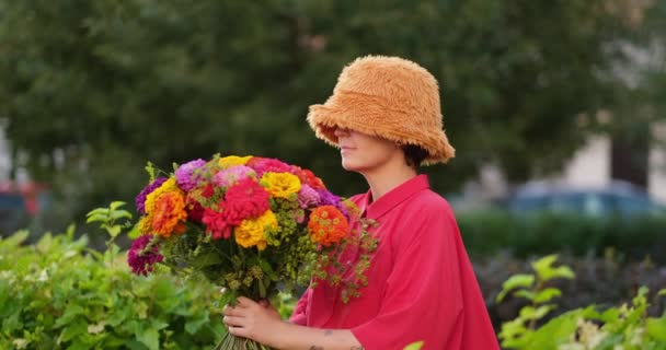 全景中的女人把脸插在五彩缤纷的花束里 滑稽的手势 在绿色花园的背景上举着一束红色 橙色和黄色的菊花 高质量的4K视频镜头 — 图库视频影像