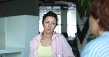Ofiste konuşan ve masada oturup kahve içen iki bayan meslektaşım. Bir kadın bir şeyi jestle açıklıyor. Yüksek kalite 4k görüntü