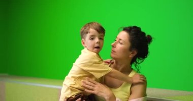 Anne ve küçük oğlu yeşil arka planda oynayıp eğleniyorlar. Küçük çocuk 15 yaşında, annesinin kollarıyla oynuyor. Yüksek kalite 4k görüntü