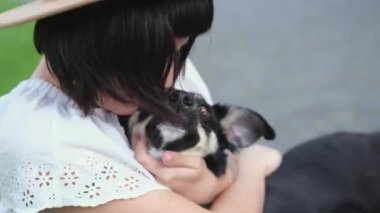 Bahçedeki çimlerin üzerinde oturan güzel genç kadın ve köpek. Gülümsüyor ve köpeğe sarılıyor. Eski şehir manzarası. Yüksek kaliteli görüntüler 4K