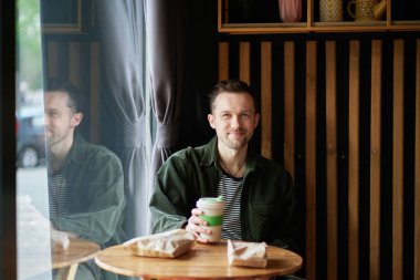 Kahve molasında bir kafede oturan genç adam. Kameraya bakıyorum. Küçük bir kafede iyi vakit geçiriyorum. Yüksek kaliteli bir fotoğraf.