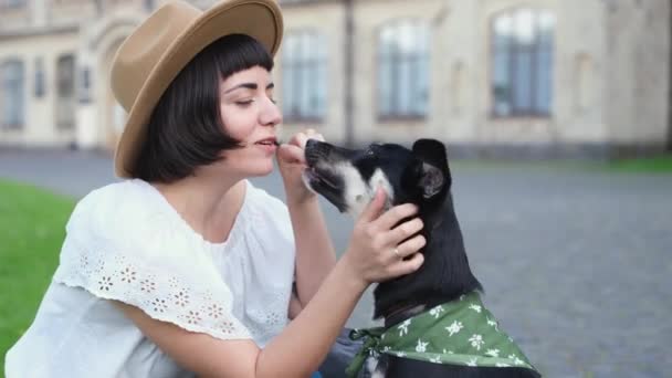 裏庭の草の上に座っているかなり若い女性と犬 笑顔で犬を抱きしめる 旧市街の風景 高品質の映像 — ストック動画