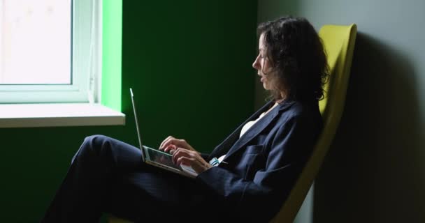暗い背景で共同作業のオープンオフィス空間で作業プロセス中にノートパソコンを感情的に話して見てビジネススーツの女性のプロフィールショット 高品質の映像 — ストック動画