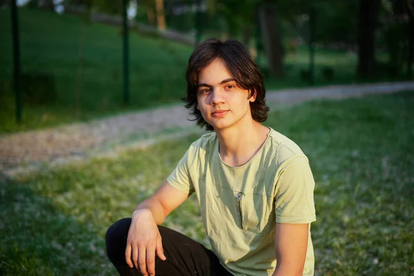 一个年轻英俊 积极的青少年穿着休闲的米黄色T恤 看着相机 一个人站在室外夕阳西下 高质量的照片 图库图片
