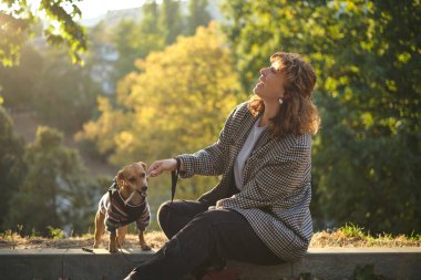 Sonbahar parkında gün batımında köpek eğitimi. Rahat giysiler içinde beyaz mutlu bir kadın konsantre dachshund köpeğiyle dışarıda oynuyor. Yüksek kaliteli dikey fotoğraf