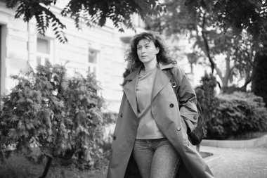 Genç, modaya uygun, modaya uygun, güzel, sıradan bir kadın sırt çantasıyla şehir caddesinde yürüyor. Kadın portresi, buluşmak için acele eden kot pantolon ve trençkot giyiyor. Yüksek kalite fotoğraf