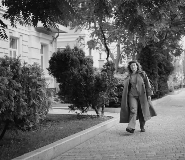 Genç, modaya uygun, modaya uygun, güzel, sıradan bir kadın sırt çantasıyla şehir caddesinde yürüyor. Kadın portresi, buluşmak için acele eden kot pantolon ve trençkot giyiyor. Yüksek kalite fotoğraf