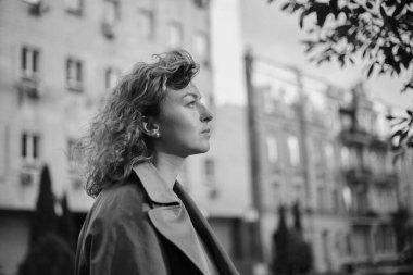 Genç, çekici, başarılı bir iş kadını, özgüvenle eski şehir manzarasının arka planına bakıyor. Akşam güneşi, kahverengi saç ve trençkot. Güven kavramı. Yüksek kalite fotoğraf