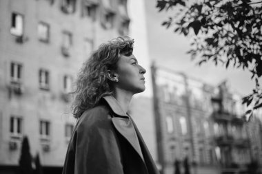 Genç, çekici, başarılı bir iş kadını, özgüvenle eski şehir manzarasının arka planına bakıyor. Akşam güneşi, kahverengi saç ve trençkot. Güven kavramı. Yüksek kalite fotoğraf