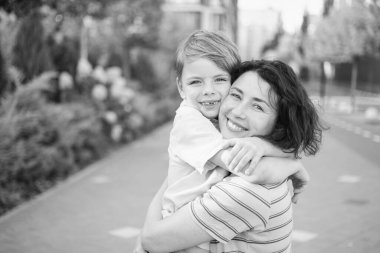 Modern mesken kompleksinde kameraya gülümseyen genç anne ve oğul. Birlikte eğlenmek, mutlu ebeveynlik, yeni ev konsepti. Şehir arka planında parlak bir yaz günü. Yüksek kalite fotoğraf