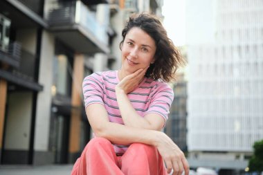 Dışarıda yürüyen mutlu genç bir kadın. Kendine güvenen bir kız sokakta gülümsüyor. Şehir merkezi, konut kompleksi, emlak konsepti. Pembe elbiseli esmer bir kadın. Yüksek kalite fotoğraf