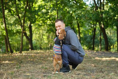 Parkta süveter giyen, beslenen, gülümseyen sevimli köpek yavrusu olan bir adam. Bahar, yaz, sonbahar yakışıklı adam dışarıda köpeğiyle eğleniyor. Mesaj için yer var. Yüksek kalite fotoğraf