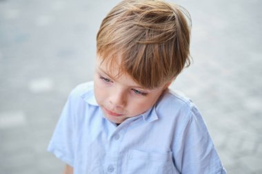 Güneşli şehir geçmişinde güzel gülümseyen küçük bir çocuk. Yakın plan portre. Sarı saçlı, mavi gözlü, 9 yaşında gülümseyen, şehirde eğlenen bir çocuk. Yüksek kalite fotoğraf