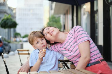 Genç anne ve oğlu yaz günü açık hava restoranında tatlı yiyorlar. Birlikte oturuyoruz, sarılıp gülüyoruz, hafta sonunun tadını çıkarıyoruz. Yüksek kalite fotoğraf