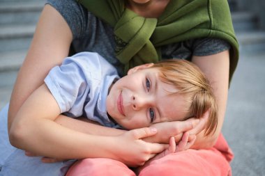 Annesine sarılan, yeşil arka plandaki kameraya bakan küçük sevimli bir çocuk. Annelik ebeveynlik kavramı, yaz havası, mutluluk. Yüksek kalite fotoğraf