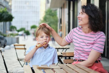 Genç anne ve oğlu yaz günü açık hava restoranında tatlı yiyorlar. Birlikte oturuyoruz, sarılıp gülüyoruz, hafta sonunun tadını çıkarıyoruz. Yüksek kalite fotoğraf