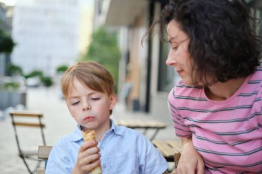 Genç anne ve oğlu yaz günü açık hava restoranında tatlı yiyorlar. Birlikte oturuyoruz, sarılıp gülüyoruz, hafta sonunun tadını çıkarıyoruz. Yüksek kalite fotoğraf