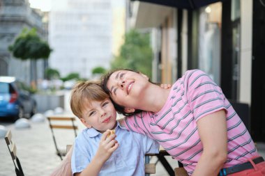 Genç anne ve oğlu yaz günü açık hava restoranında tatlı yiyorlar. Birlikte oturuyoruz, sarılıp gülüyoruz, hafta sonunun tadını çıkarıyoruz. Yüksek kalite fotoğraf
