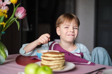 Ufaklık kahvaltıda çay ve elmalı krep yiyor. Tatlı yemekler ve duygusal çocukla şirin bir hafta sonu. Yüksek kalite fotoğraf