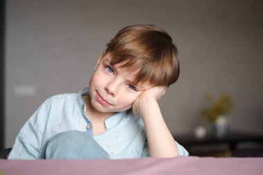 Sevimli küçük çocuk kameraya bakıyor evde oturmuş gülümsüyor ve parmağını gösteriyor. Hafta sonu ev kavramında eğleniyorum. Yüksek kalite fotoğraf