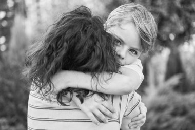 Annesine sarılan, yeşil arka plandaki kameraya bakan küçük sevimli bir çocuk. Annelik ebeveynlik kavramı, yaz havası, mutluluk. Yüksek kalite fotoğraf