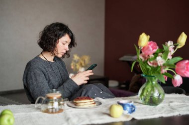 Evde masada çay ve kreplerle oturan orta yaşlı kadınlar. Akıllı telefon kullanıyor. Kameraya bakan, gülümseyen, sıradan kıyafetler giyen güzel bir kız. Yüksek kalite fotoğraf