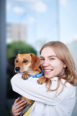 Veteriner kliniğinin girişinde gülümseyen ve köpeği tutan genç bir veteriner. Sağlıklı köpek, teşhis, evcil hayvan tedavisi. Yüksek kalite fotoğraf