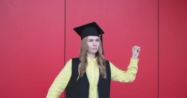 Mezuniyet şapkalı güzel sarışın kadın. Kırmızı arka planda duygusal bir yüz ifadesi var. Okulu, üniversiteyi ya da üniversiteyi bitirmekten mutluluk duyarım.