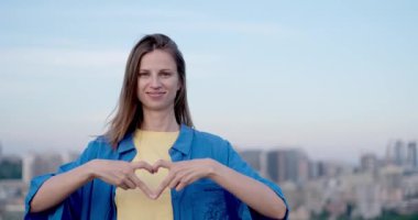 Ukrayna 'nın ulusal renkleri içinde genç bir kadın Kyiv şehrinin manzarasına sevgi yolluyor. Bağımsız kavram, Ukrayna 'yı desteklemek, savaşı durdurmak. Yüksek kalite fotoğraf