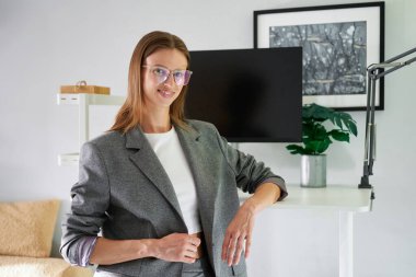 Ofis arka planında gülümseyen gözlüklü ve gri takım elbiseli genç bir bayan. HR ya da CEO kadın, katman, belki gayrimenkul. Yüksek kalite fotoğraf