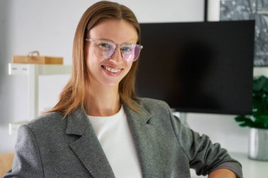 Ofis arka planında gülümseyen gözlüklü ve gri takım elbiseli genç bir bayan. HR ya da CEO kadın, katman, belki gayrimenkul. Yüksek kalite fotoğraf