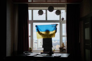 Bir dikiz aynası, Ukrayna bayrağını gururla taşıyan ve vatanseverliğini vurgulayan bir kadını evinin penceresinin yanında yakalıyor. Şehre bakıyorum, savaşın getirdiği yüksek kaliteli fotoğrafı düşünüyorum.