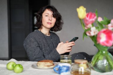 Evde masada çay ve kreplerle oturan orta yaşlı kadınlar. Akıllı telefon kullanıyor. Kameraya bakan, gülümseyen, sıradan kıyafetler giyen güzel bir kız. Yüksek kalite fotoğraf