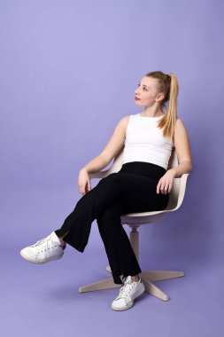 Beautiful blond young woman sitting in a chair on a violet background