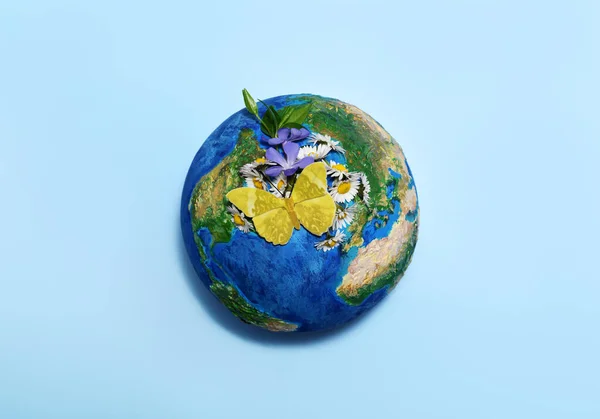 Earth globe with flowers and butterfly on light blue background