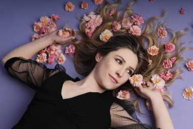 Güzel sarışın kadın menekşe arka planda pembe güllerle yatıyor.