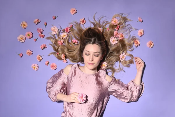 stock image Beutiful blond woman lying with pink roses on violet background