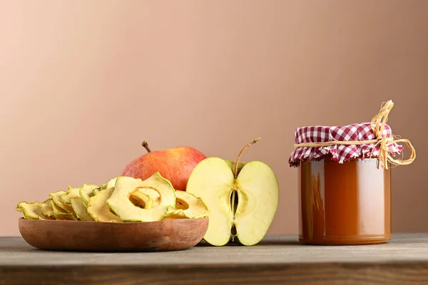 Jar of jam, plate with apple chips and fresh apples on beige background