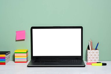 Beyaz ekranlı dizüstü bilgisayar ve yeşil arka planda ofis aksesuarları