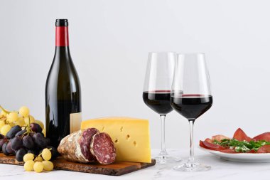 İki kadeh kırmızı şarap, şişe ve bir tabak üzüm, İtalyan peyniri, salam ve jambon.