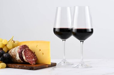 İki kadeh kırmızı şarap, üzümlü pansiyon, İtalyan peyniri ve salam. 