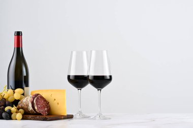 İki kadeh kırmızı şarap, şişe ve bir tabak üzüm, İtalyan peyniri ve salam.