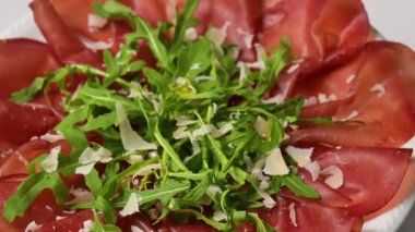 İtalyan jambonlu bresaola üzerine roka ve parmesan peyniri dökülüyor.