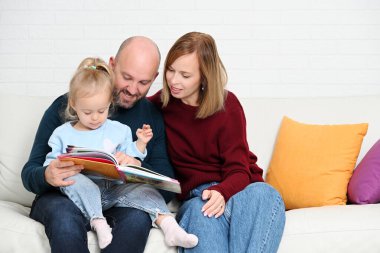 Kanepede oturup kitap okuyan neşeli bir aile.