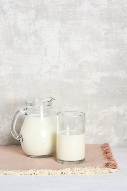 Tahta masada bir bardak süt ve sürahi ve arka planda gri duvar