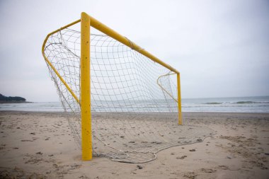 Parlak sarı bir futbol kalesi kumlu bir plajda, arka planda uzanan engin okyanusla, pitoresk bir sahne yaratıyor.