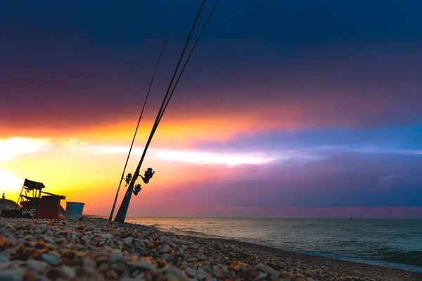 Beautiful sunset over the sea. Fishing rods on the shore of the sea against the background of a dramatic sunset. Night fishing.