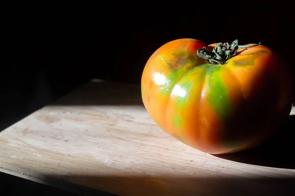 新鲜多汁的红色西红柿 绿色斑点 与伦勃朗的阳光相反 一个孤立的蔬菜在木制表面的黑色背景 生物素食无麸质营养概念 — 图库照片